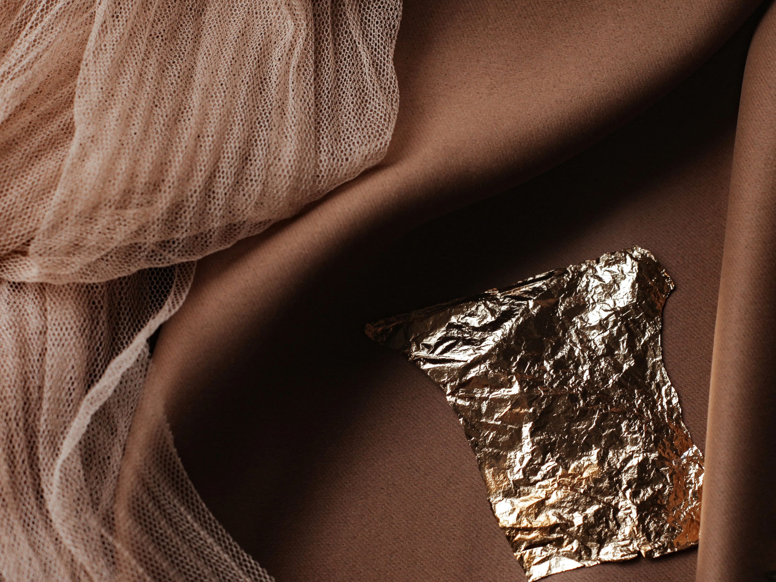 Artistic composition featuring draped fabrics and a piece of gold foil on a dark backdrop.